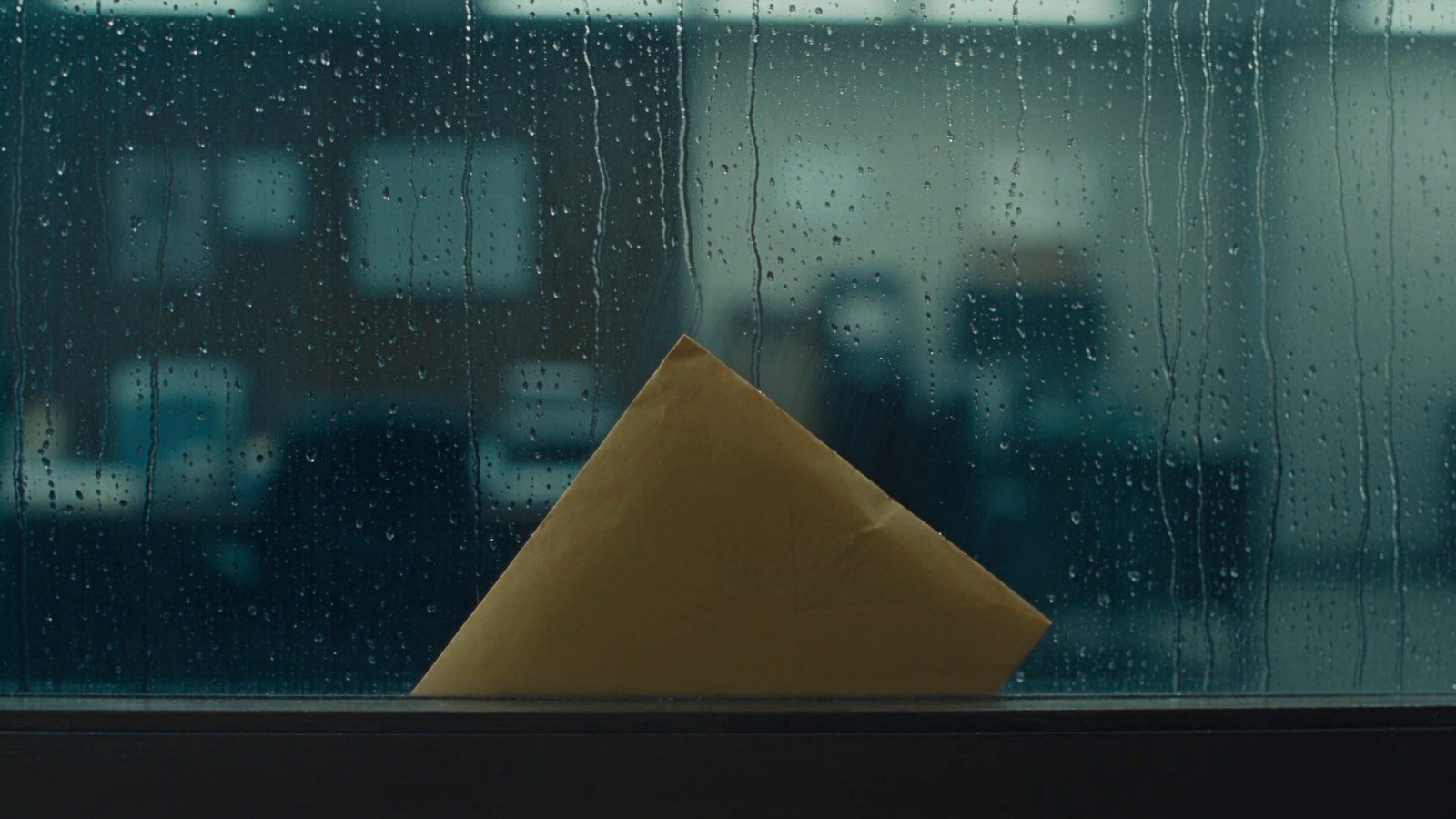 A wet yellow envelope pressed against the outside of a rain-streaked office window.